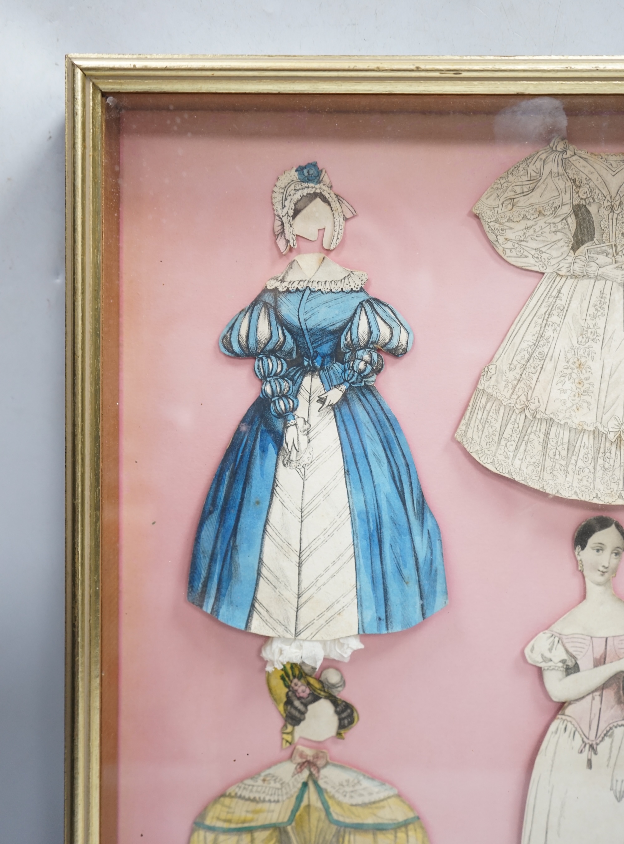 An early 19th century framed Rudolph Ackermann La Poupee-Modele paper doll set, comprising of a double sided doll in lingerie with wooden stand, five double sided gowns and five bonnets, dimensions of the frame; 40cm wid